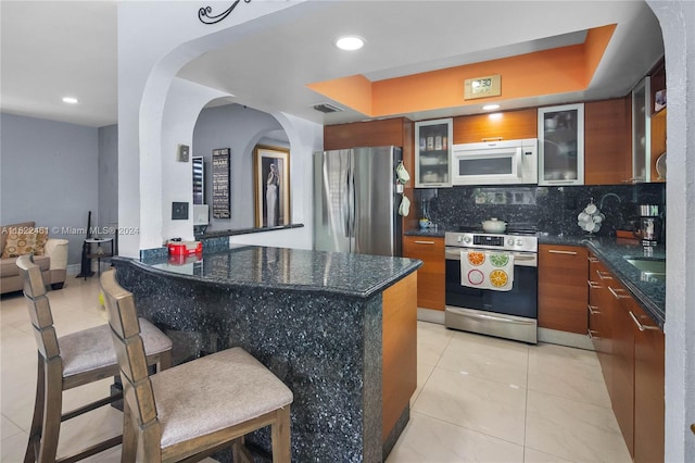 kitchen with dark stone counters, a kitchen breakfast bar, backsplash, light tile patterned floors, and stainless steel appliances