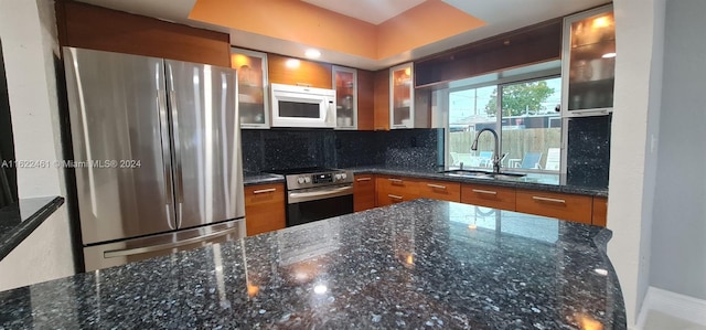 kitchen with decorative backsplash, a tray ceiling, sink, dark stone countertops, and stainless steel appliances