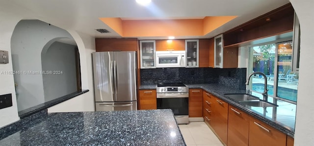 kitchen featuring decorative backsplash, dark stone counters, light tile patterned floors, sink, and stainless steel appliances