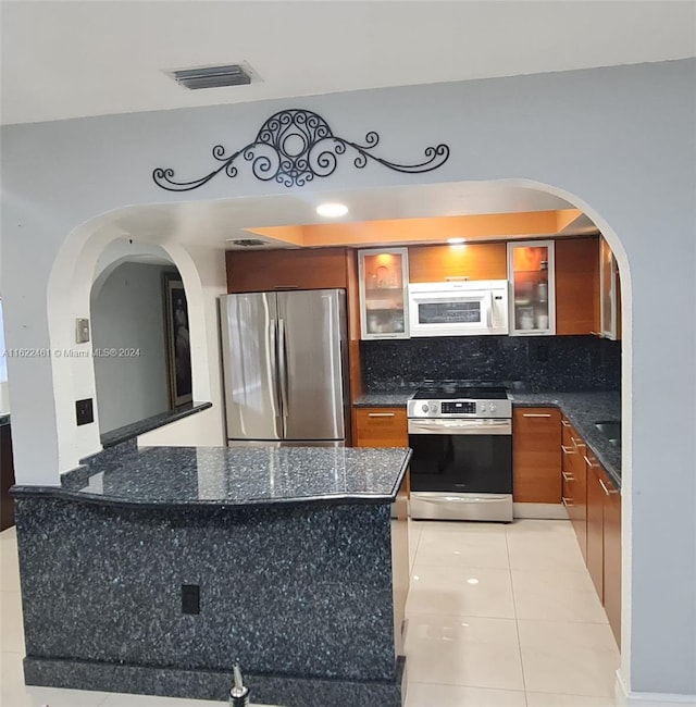 kitchen with light tile patterned floors, appliances with stainless steel finishes, dark stone countertops, and decorative backsplash