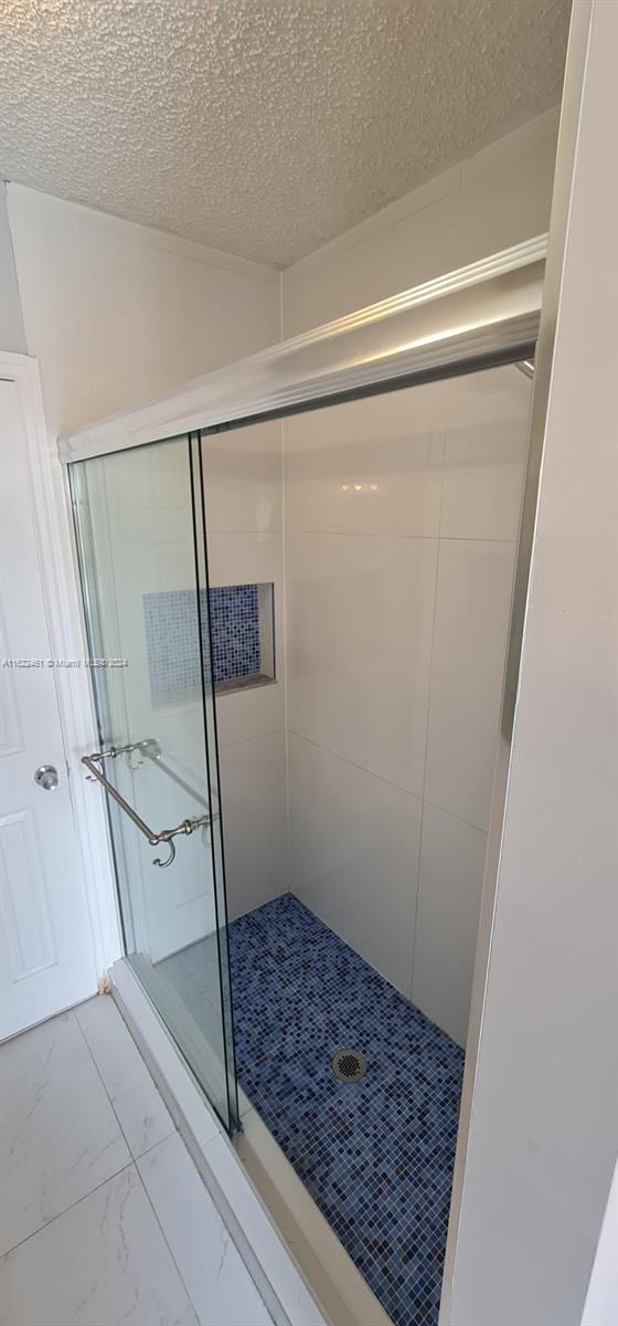 bathroom featuring a textured ceiling, a shower with shower door, and tile patterned floors