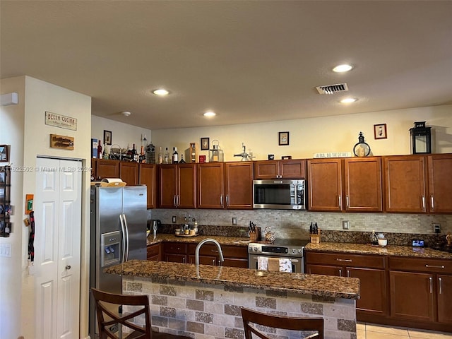 kitchen featuring stainless steel appliances, a breakfast bar, backsplash, light tile patterned floors, and a kitchen island with sink