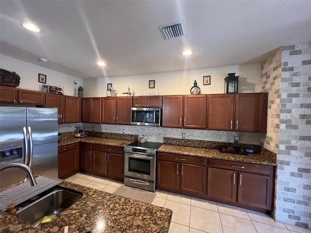 kitchen with dark stone counters, brick wall, sink, appliances with stainless steel finishes, and light tile patterned floors