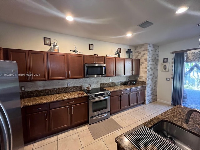 kitchen featuring appliances with stainless steel finishes, dark stone counters, sink, light tile patterned floors, and decorative backsplash