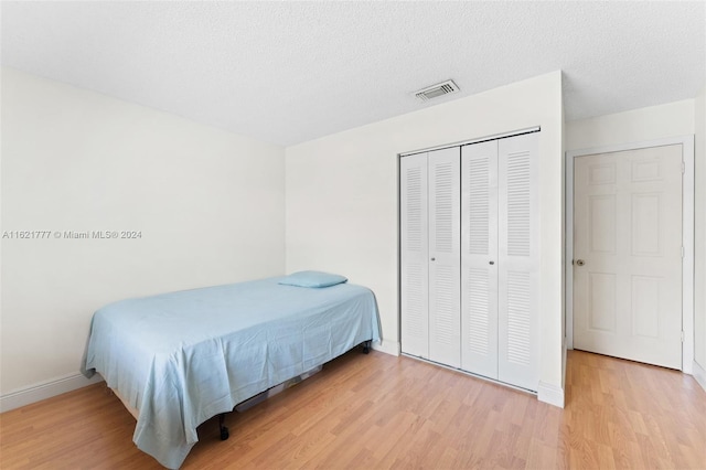 bedroom with a closet, visible vents, a textured ceiling, and wood finished floors