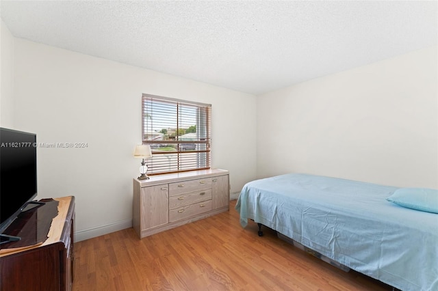 bedroom featuring light wood-type flooring, a textured ceiling, and baseboards