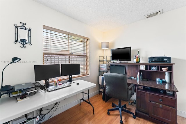 office area with light wood finished floors, baseboards, visible vents, and a textured ceiling