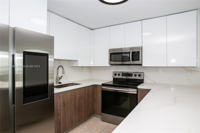 kitchen with light stone countertops, white cabinets, appliances with stainless steel finishes, sink, and light tile patterned floors