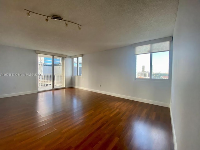 empty room with track lighting, a textured ceiling, wood-type flooring, and a healthy amount of sunlight