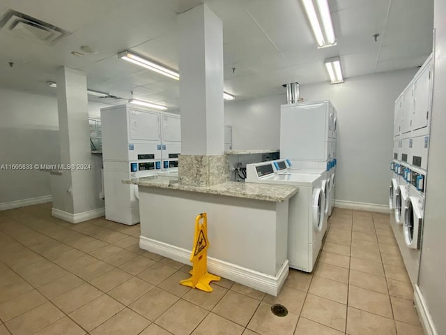 kitchen featuring white cabinetry, stacked washer / dryer, light tile patterned floors, kitchen peninsula, and washing machine and clothes dryer