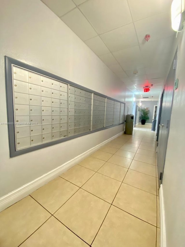 hallway with mail boxes, light tile patterned floors, and a paneled ceiling