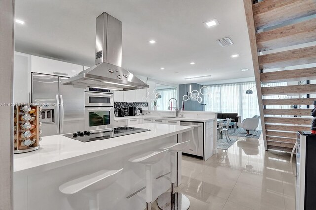 kitchen featuring island exhaust hood, appliances with stainless steel finishes, backsplash, kitchen peninsula, and sink