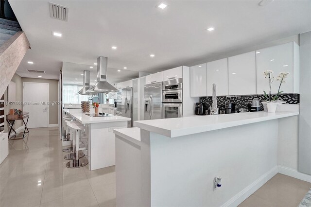 kitchen with a kitchen breakfast bar, stainless steel appliances, island range hood, a center island, and white cabinetry