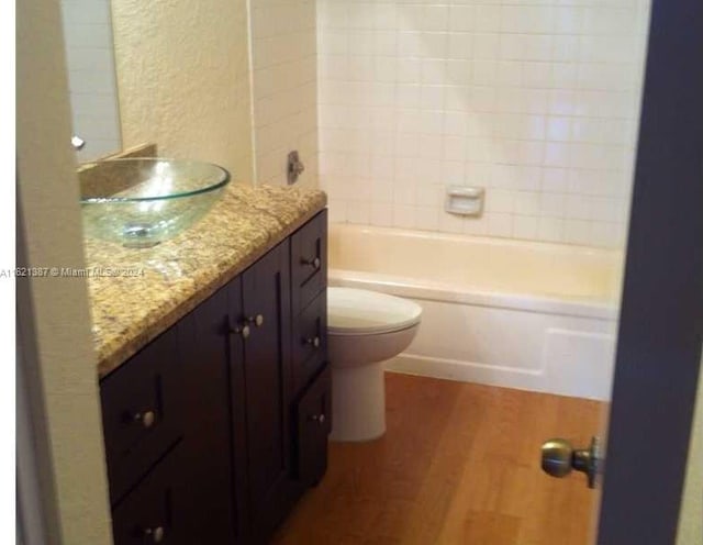 full bathroom with vanity, hardwood / wood-style flooring, tiled shower / bath, and toilet