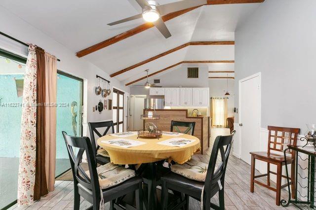 dining room with light wood-type flooring, ceiling fan, and vaulted ceiling with beams