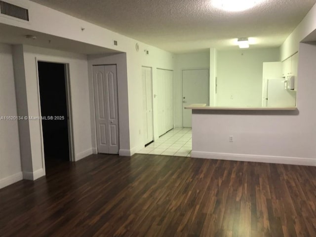 unfurnished room with visible vents, a textured ceiling, baseboards, and wood finished floors