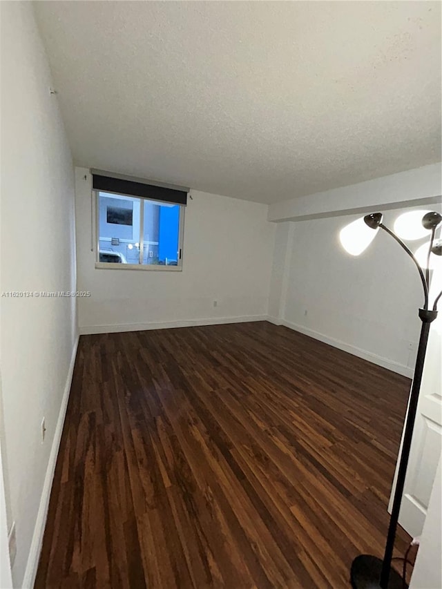 spare room featuring dark wood finished floors, a textured ceiling, and baseboards