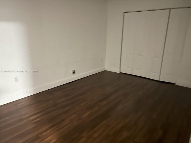 unfurnished bedroom with a closet, baseboards, and dark wood-style floors