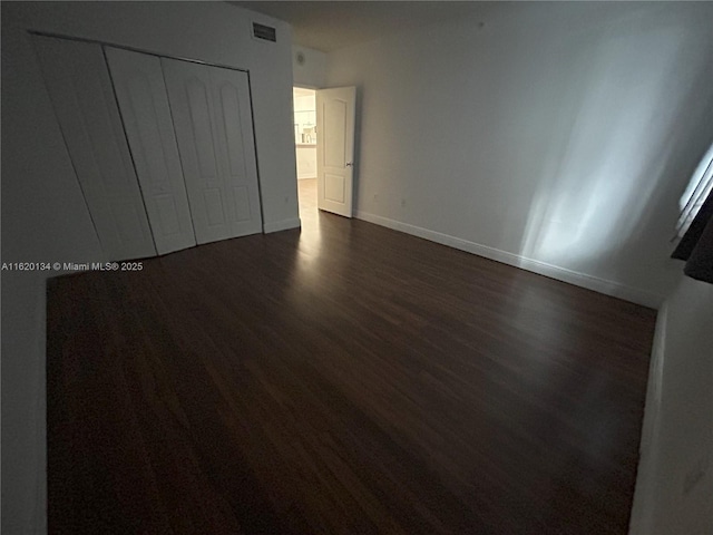 unfurnished bedroom featuring dark wood-type flooring, visible vents, baseboards, and a closet