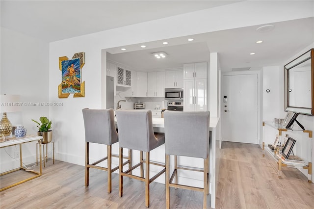 kitchen with light wood-type flooring, kitchen peninsula, white cabinets, a kitchen breakfast bar, and stove