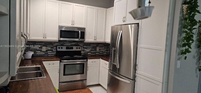 kitchen featuring appliances with stainless steel finishes, white cabinetry, tasteful backsplash, and wood counters