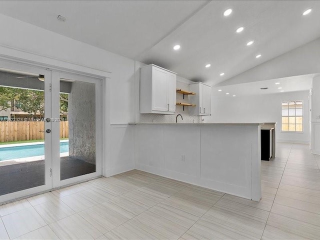 kitchen with white cabinetry, french doors, kitchen peninsula, lofted ceiling, and decorative backsplash