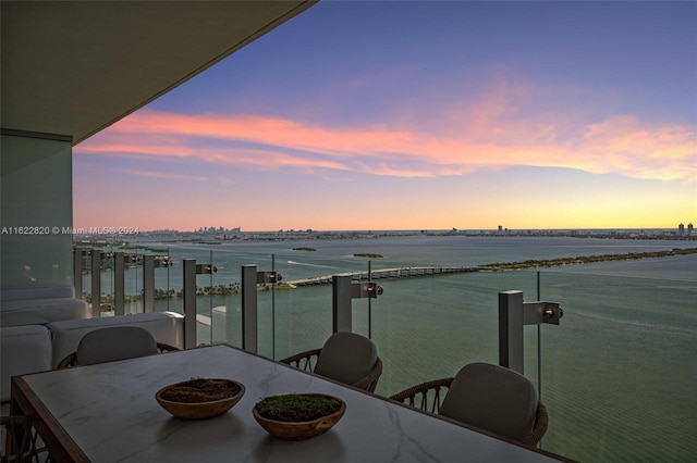 balcony at dusk featuring a water view