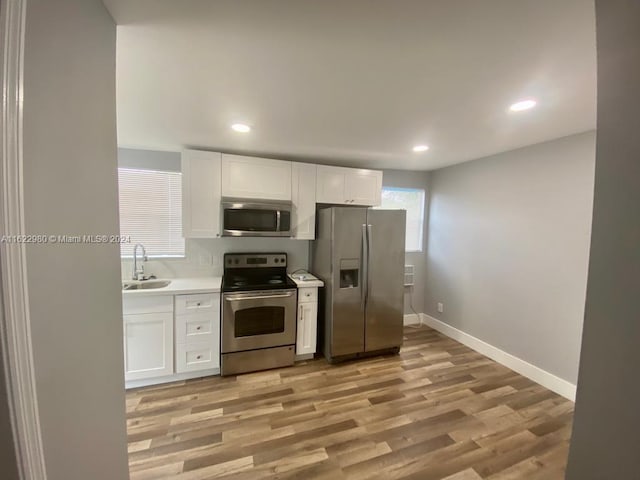 kitchen with sink, appliances with stainless steel finishes, light hardwood / wood-style flooring, and white cabinetry