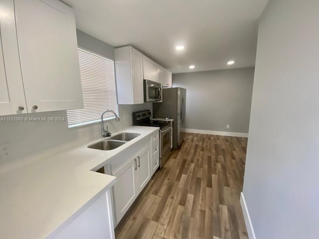 kitchen featuring appliances with stainless steel finishes, white cabinetry, hardwood / wood-style flooring, and sink