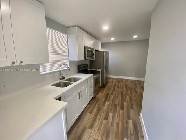 kitchen with white cabinets, hardwood / wood-style floors, appliances with stainless steel finishes, and sink