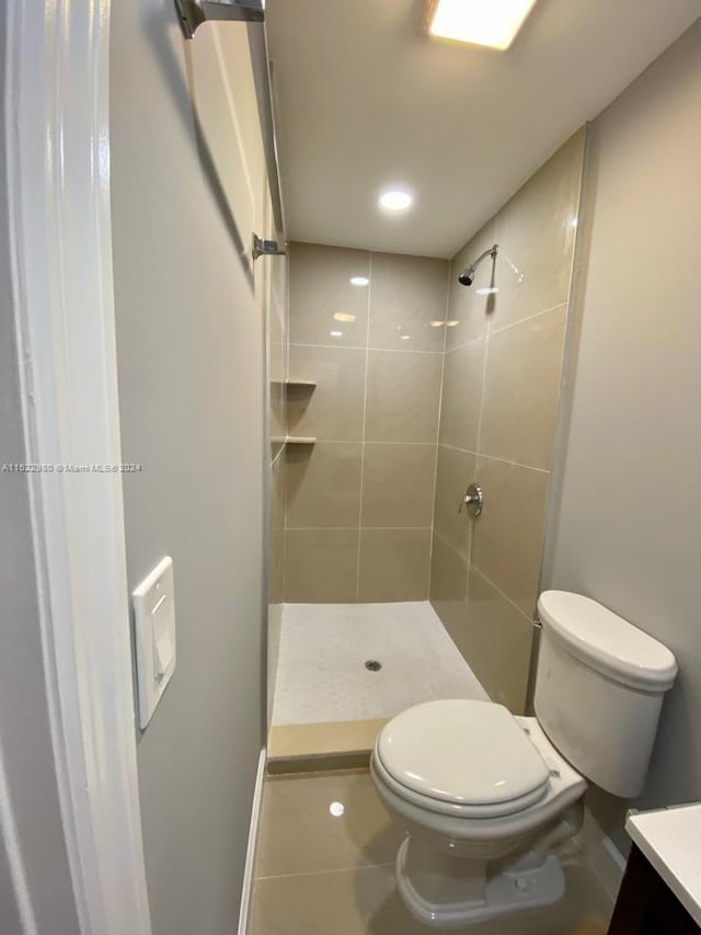 bathroom featuring vanity, tile patterned flooring, a tile shower, and toilet