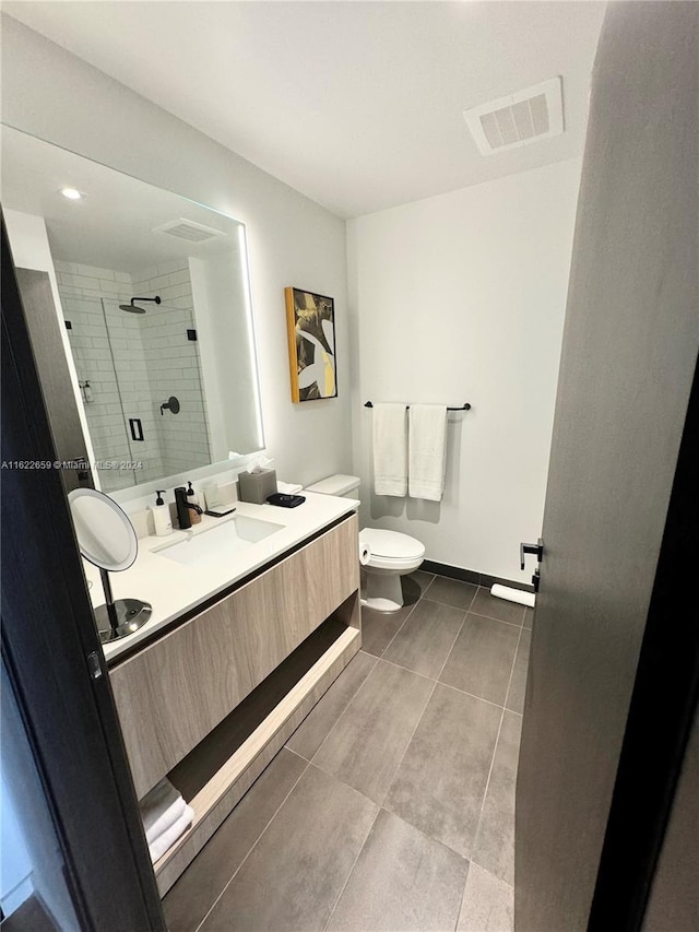 bathroom featuring tile patterned flooring, a tile shower, vanity, and toilet