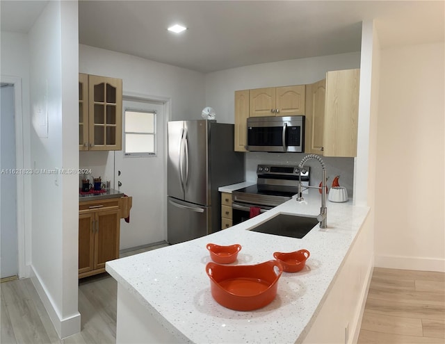 kitchen with light stone counters, sink, appliances with stainless steel finishes, and light wood-type flooring