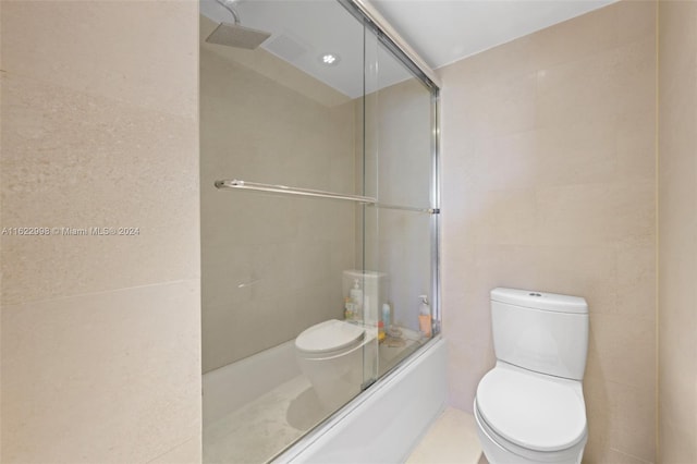 bathroom featuring tile walls, toilet, and shower / bath combination with glass door