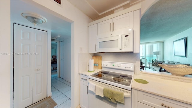 kitchen with white cabinetry, light stone countertops, light tile patterned floors, and white appliances