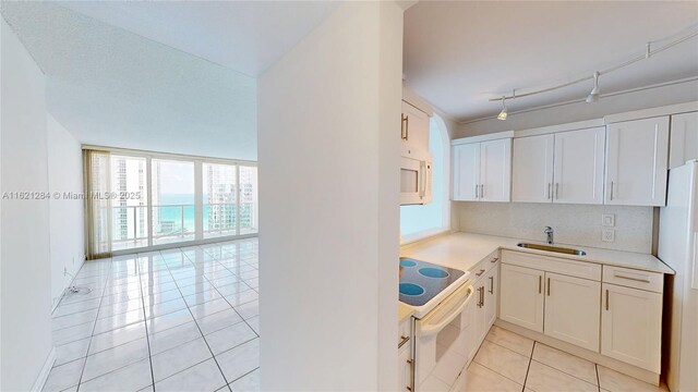 kitchen featuring light tile patterned flooring, white cabinetry, sink, a water view, and white appliances