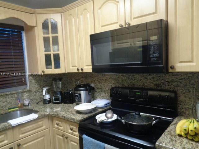 kitchen featuring cream cabinets, black appliances, and backsplash