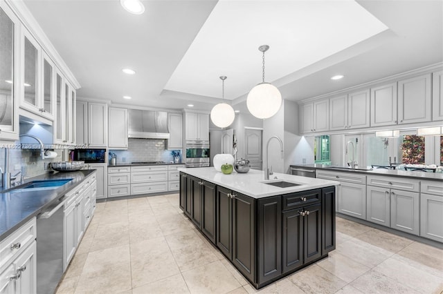 kitchen with a kitchen island with sink, a raised ceiling, sink, decorative light fixtures, and stainless steel appliances