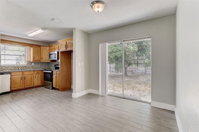 kitchen with appliances with stainless steel finishes, backsplash, light wood-type flooring, and sink