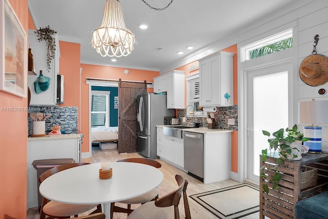 kitchen featuring stainless steel appliances, white cabinetry, a barn door, and decorative backsplash