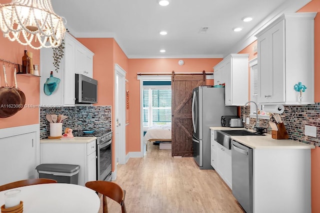 kitchen with pendant lighting, white cabinets, stainless steel appliances, light wood-type flooring, and a barn door