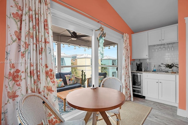 dining space featuring vaulted ceiling, indoor wet bar, light wood-type flooring, and wine cooler