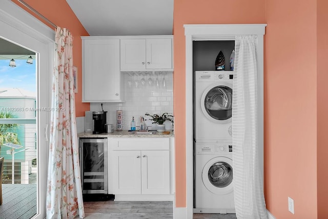 clothes washing area featuring light hardwood / wood-style floors, stacked washer / dryer, beverage cooler, and indoor wet bar