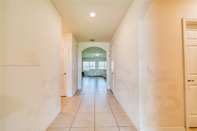 hall with arched walkways, light tile patterned floors, baseboards, and visible vents