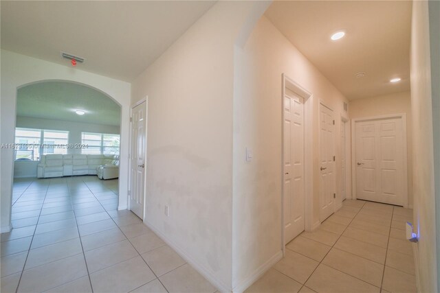 hall with light tile patterned floors, visible vents, baseboards, recessed lighting, and arched walkways