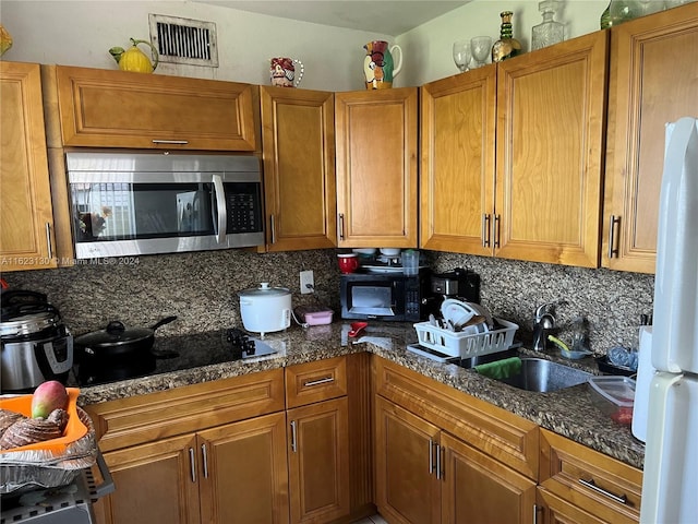 kitchen featuring backsplash, dark stone countertops, sink, and black appliances