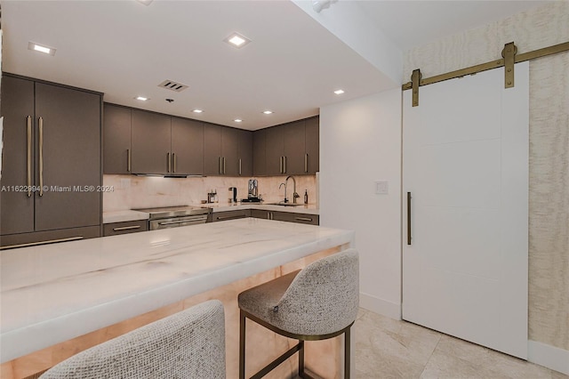 kitchen featuring tasteful backsplash, a barn door, stainless steel range oven, a kitchen breakfast bar, and sink