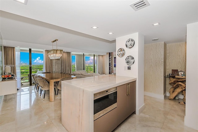 kitchen with light stone countertops, decorative light fixtures, kitchen peninsula, a chandelier, and floor to ceiling windows