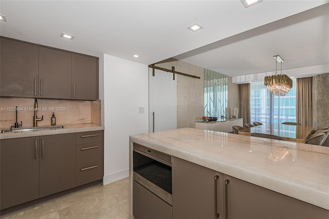 kitchen with decorative light fixtures, sink, stainless steel microwave, gray cabinetry, and a barn door