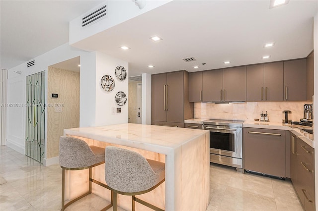 kitchen featuring stainless steel electric range, kitchen peninsula, a kitchen bar, decorative backsplash, and light stone countertops